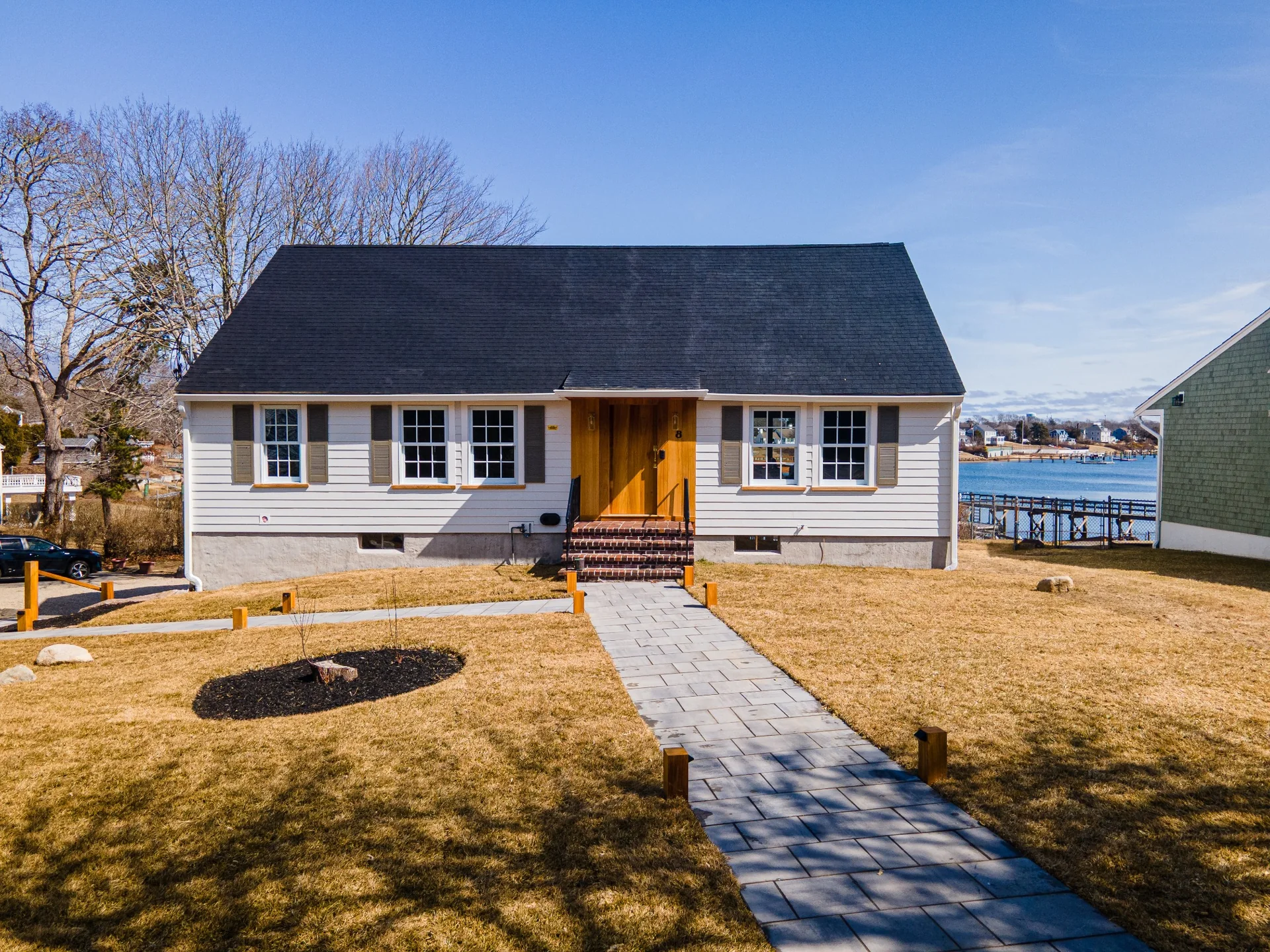 Prospera exterior renovation view with white siding, updated trim, front walkway, and a custom wood entry accent.