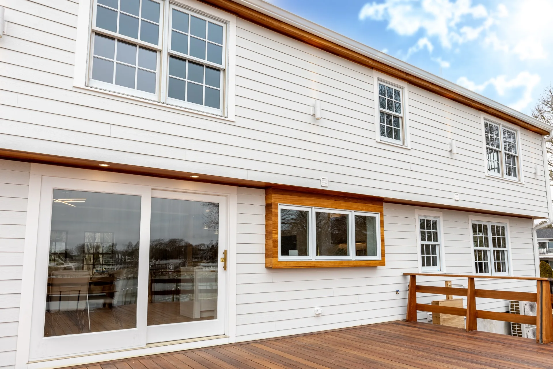 Rear home facade with custom deck woodwork, exterior stair details, railing, siding, and waterfront access.