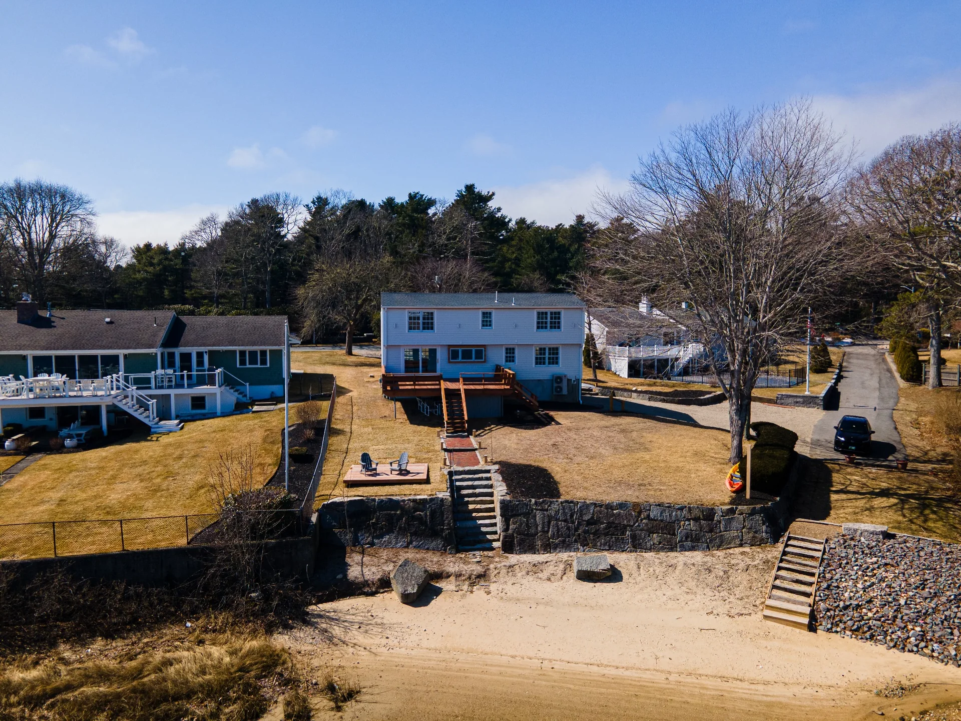 Drone view of shoreline backyard, waterfront property layout, rear deck, lawn, and exterior home improvements.