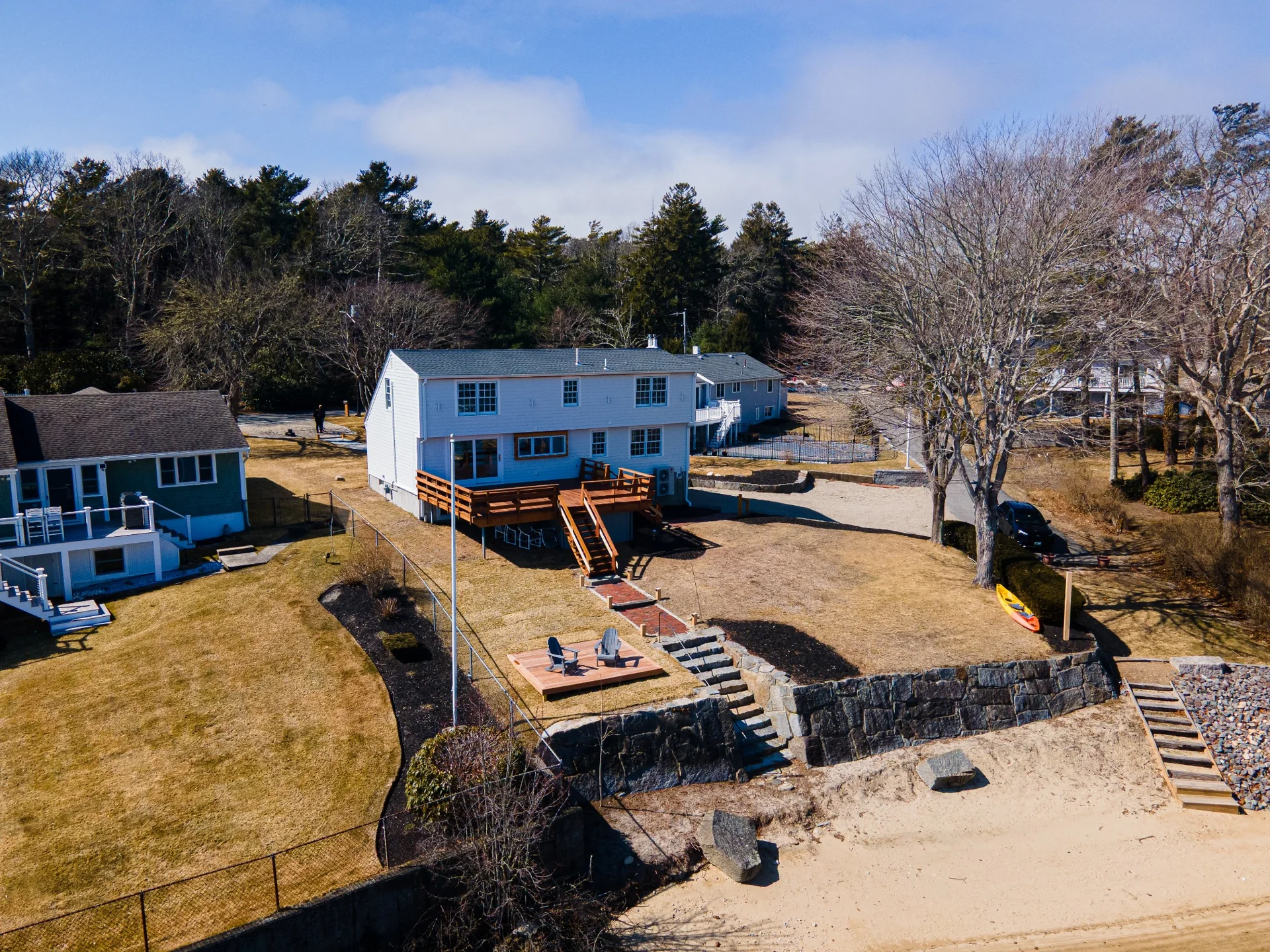 Waterfront backyard aerial image showing the completed exterior deck area, lawn, shoreline, and home facade.