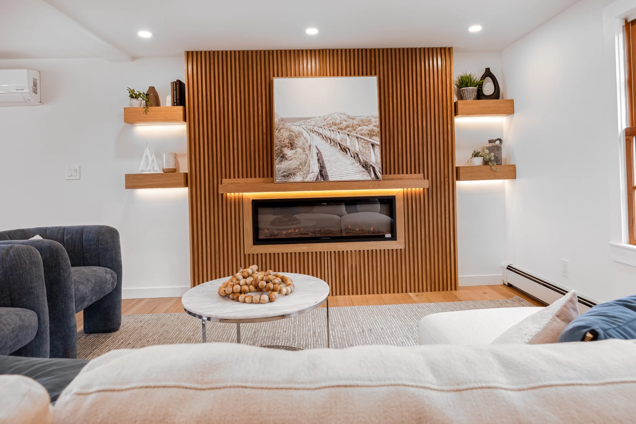 Living room feature wall with vertical wood slats, linear fireplace, floating shelves, and warm accent lighting.