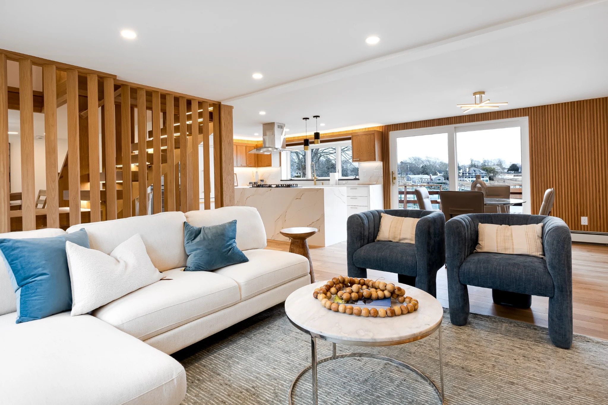 Open-concept living room with bright seating area, blue accent chairs, clean flooring, and views toward the kitchen.