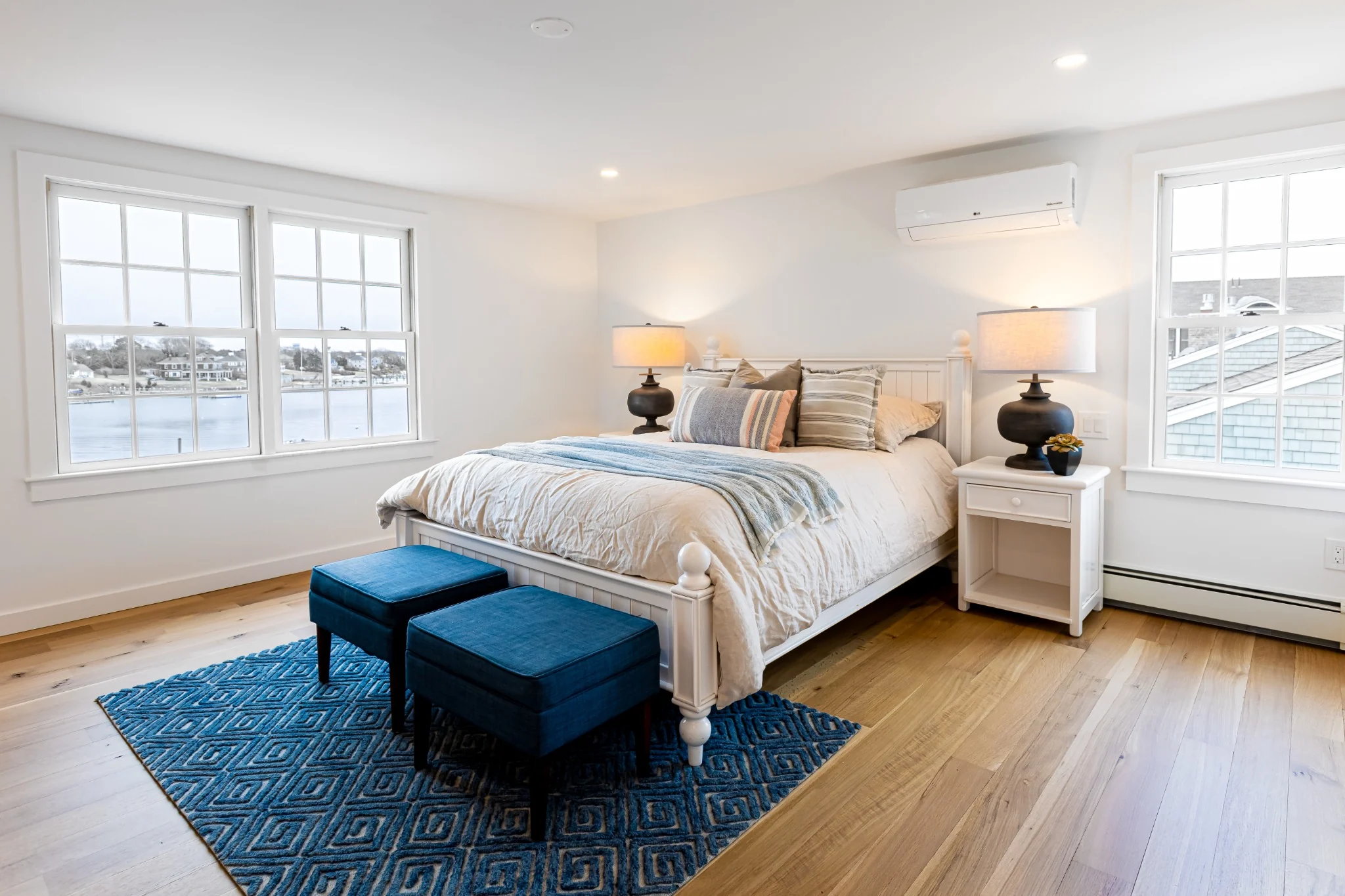 Primary bedroom with blue rug, wood bed, waterfront window view, and calm completed interior presentation.