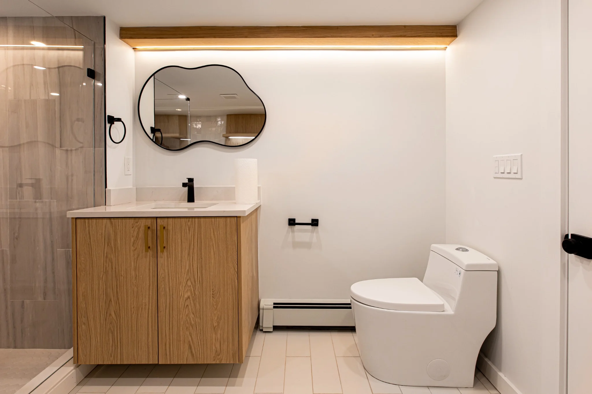 Modern bathroom with wood vanity, black fixtures, clean mirror detail, and refined interior finish work.