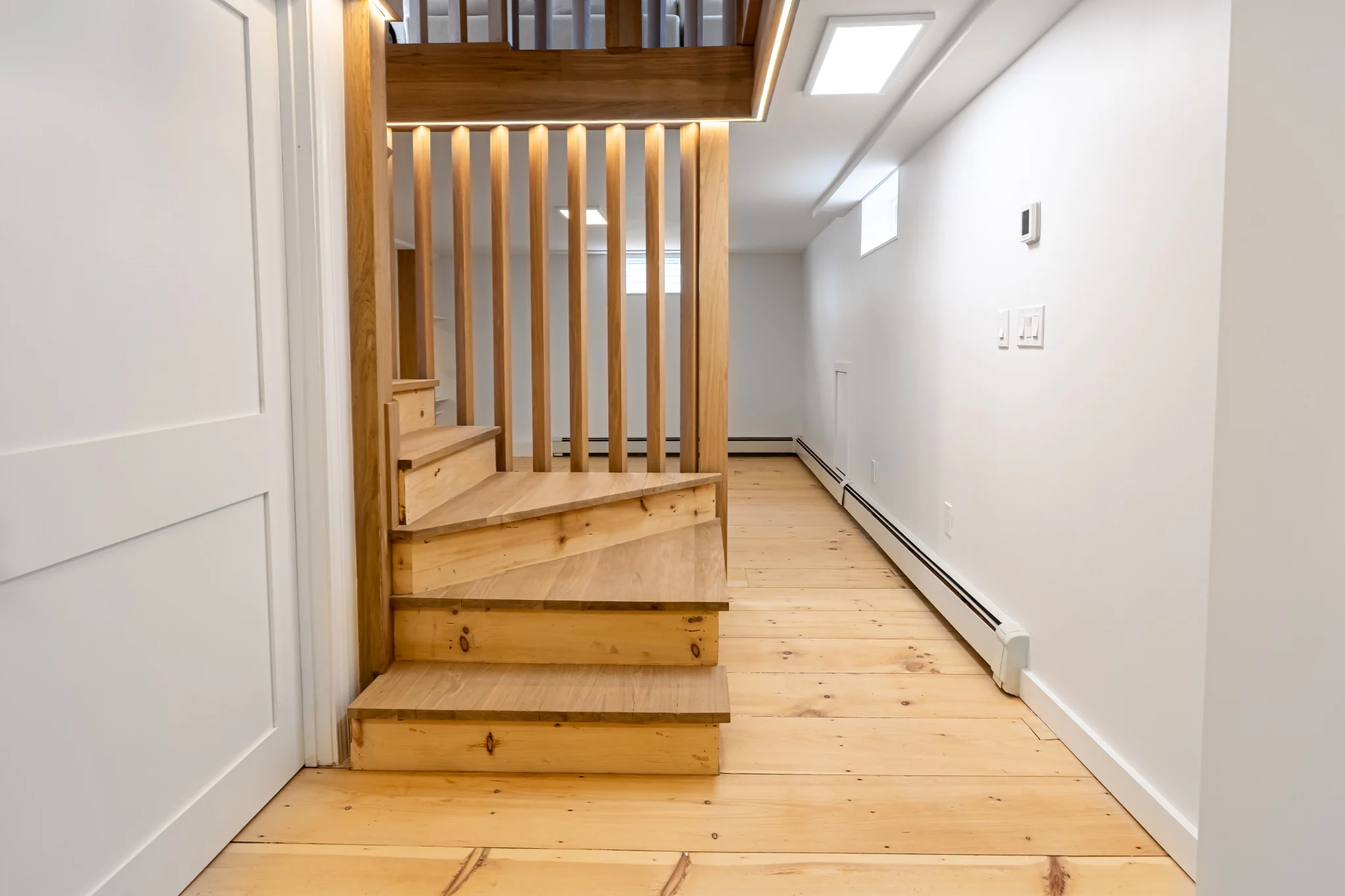 Lower-level staircase with warm wood treads, vertical slat railing, integrated accent lighting, and wood flooring.