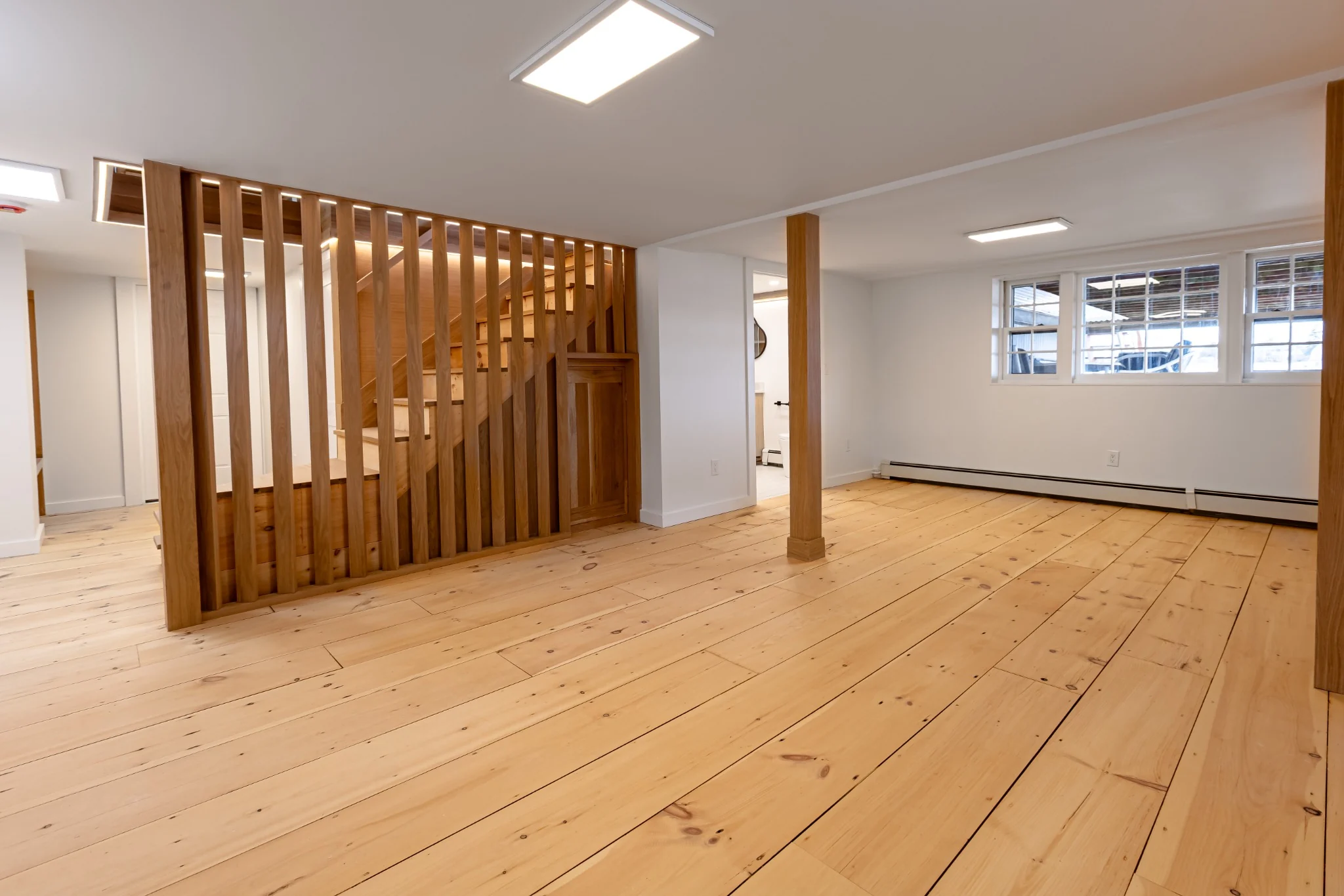 Finished basement staircase with wide plank wood flooring, wood slat wall, exposed posts, and clean white walls.