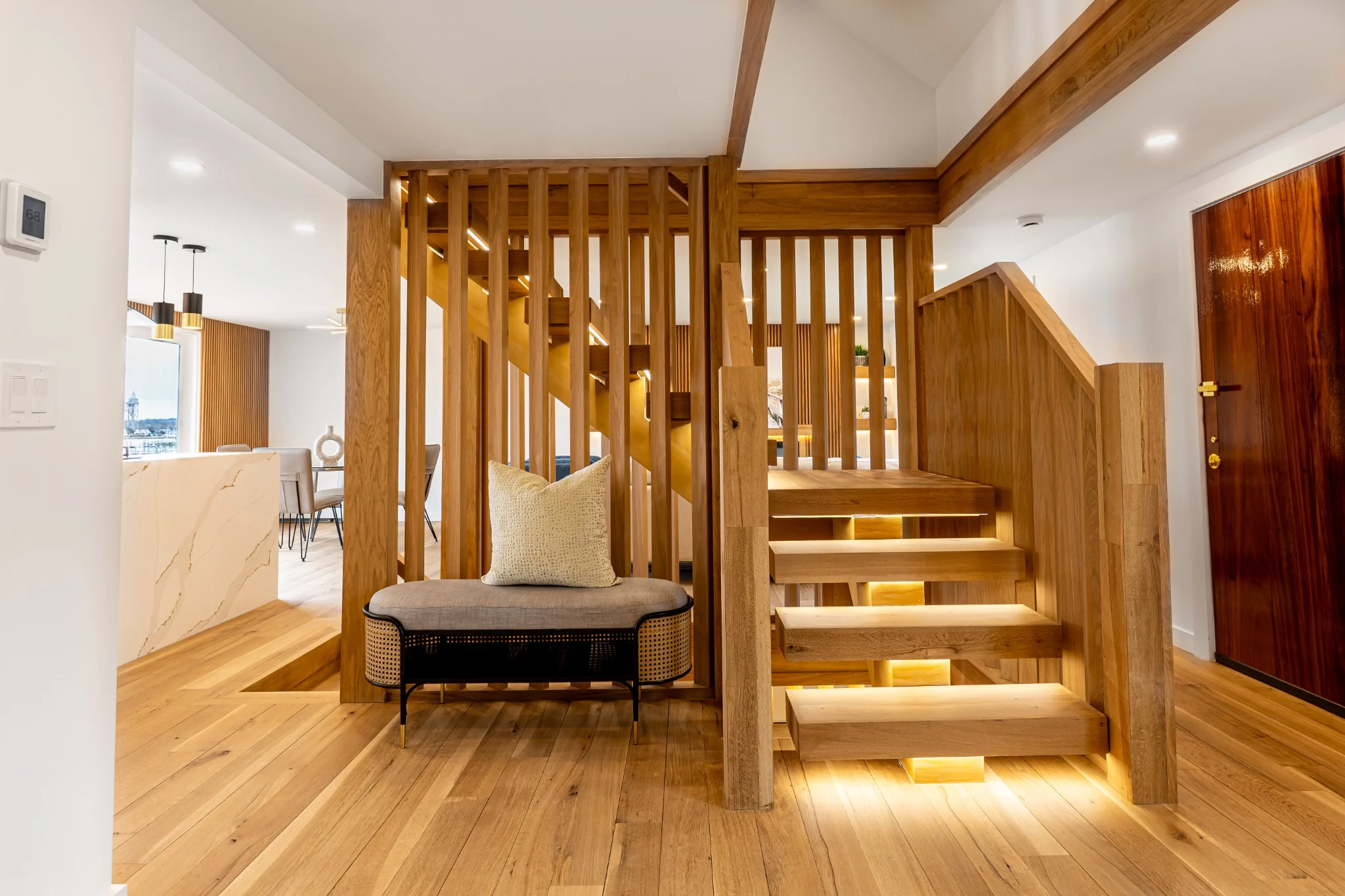 Custom oak staircase with vertical slat railing, integrated step lighting, and open-concept entry details.